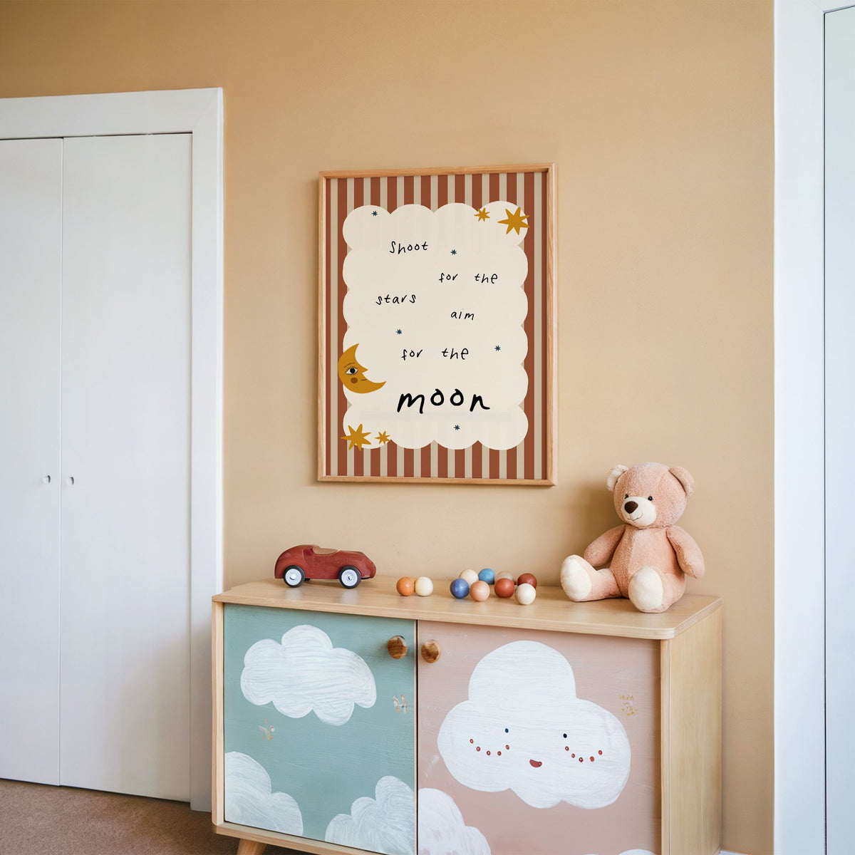 Shoot for the stars moon nursery print in an oak frame on a peach wall above a cloud-painted cabinet