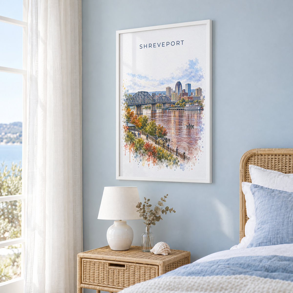 Shreveport watercolor print in a white frame on a pale blue wall beside a rattan bed in a coastal bedroom