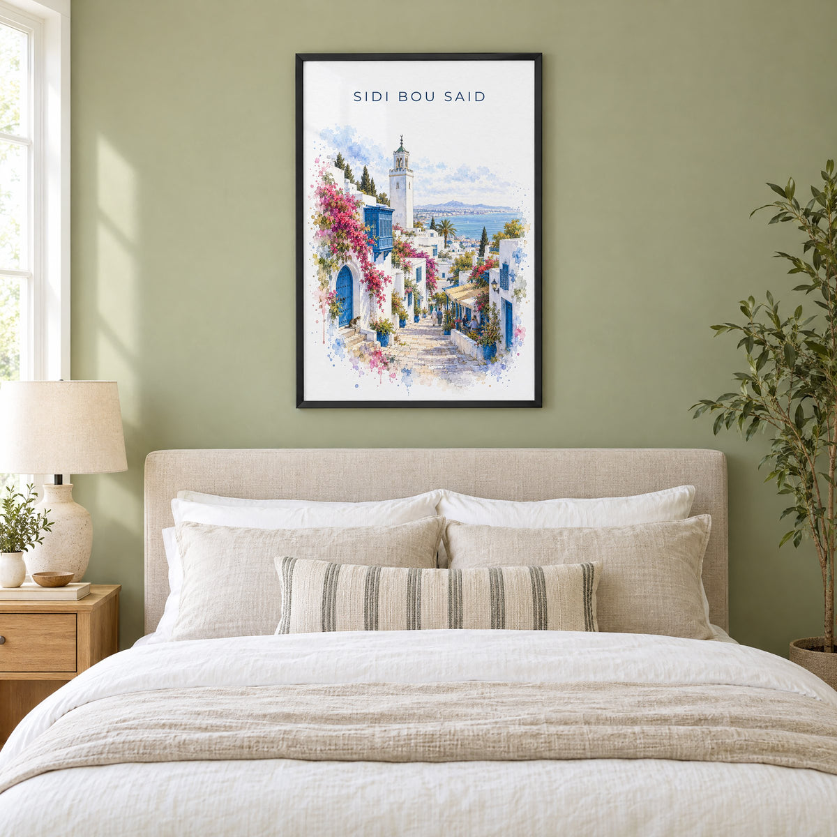 Sidi Bou Said watercolor print in a black frame above an upholstered headboard in a sage green bedroom