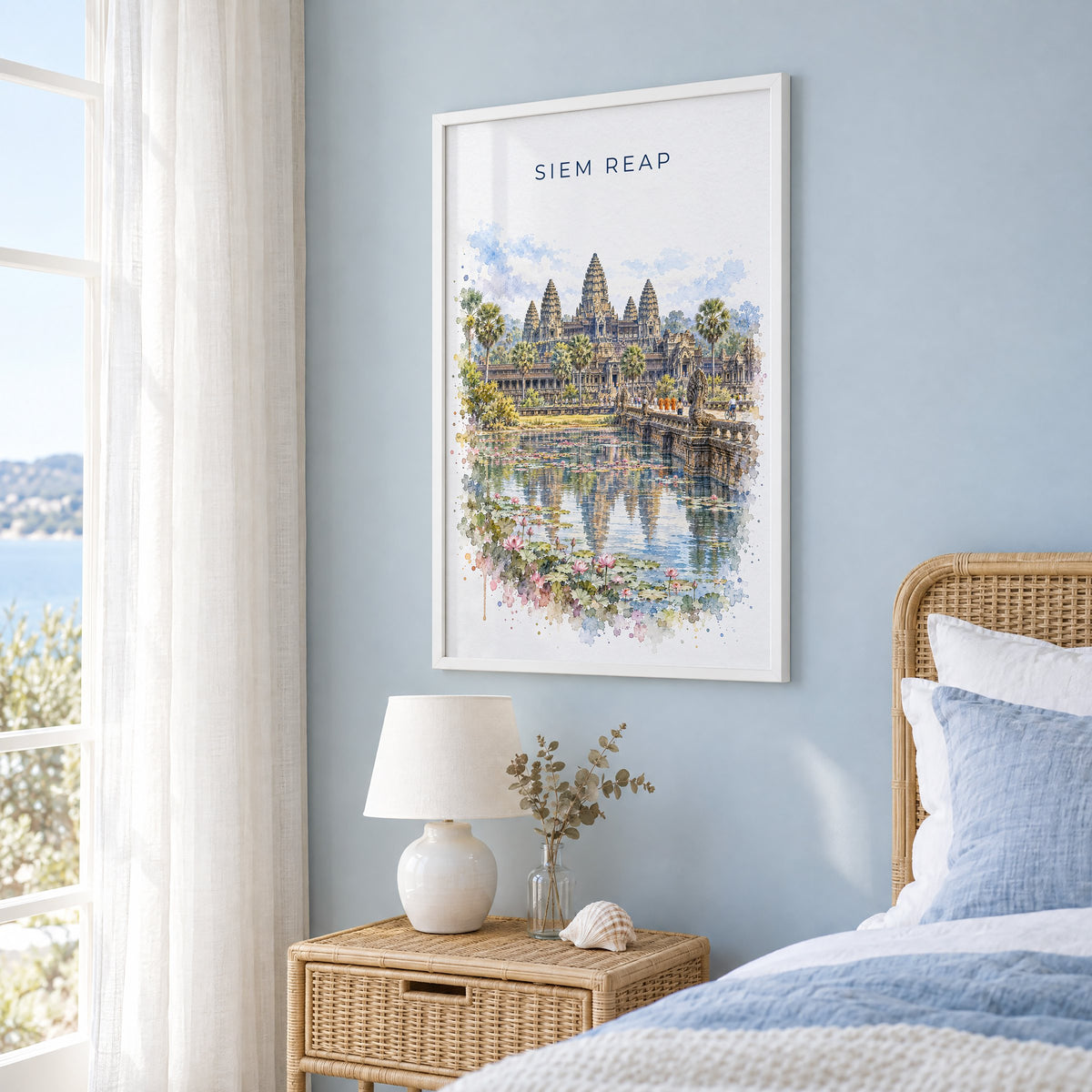 Siem Reap watercolor print in a white frame on a pale blue wall beside a rattan bed in a coastal bedroom