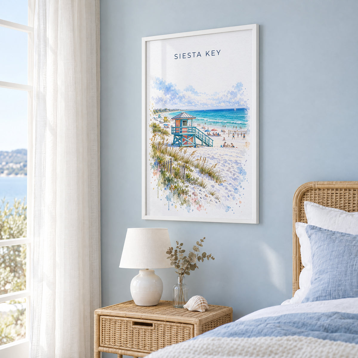 Siesta Key watercolor print in a white frame on a pale blue wall beside a rattan bed in a coastal bedroom