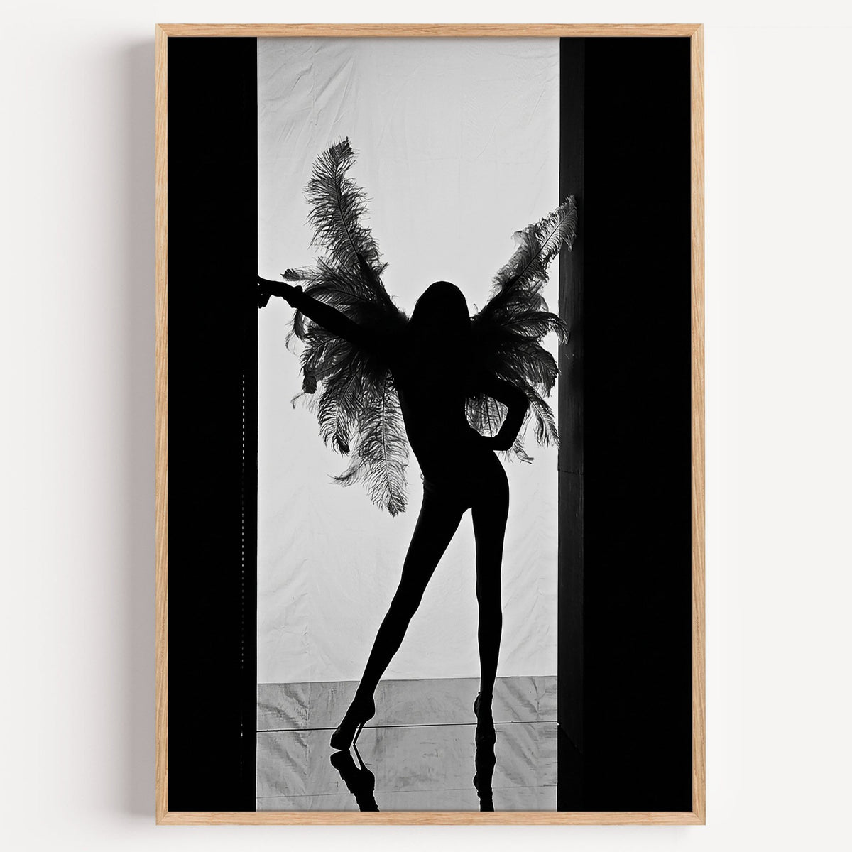 Backlit figure with feather wings in a doorway print in a light oak frame on a plain white wall