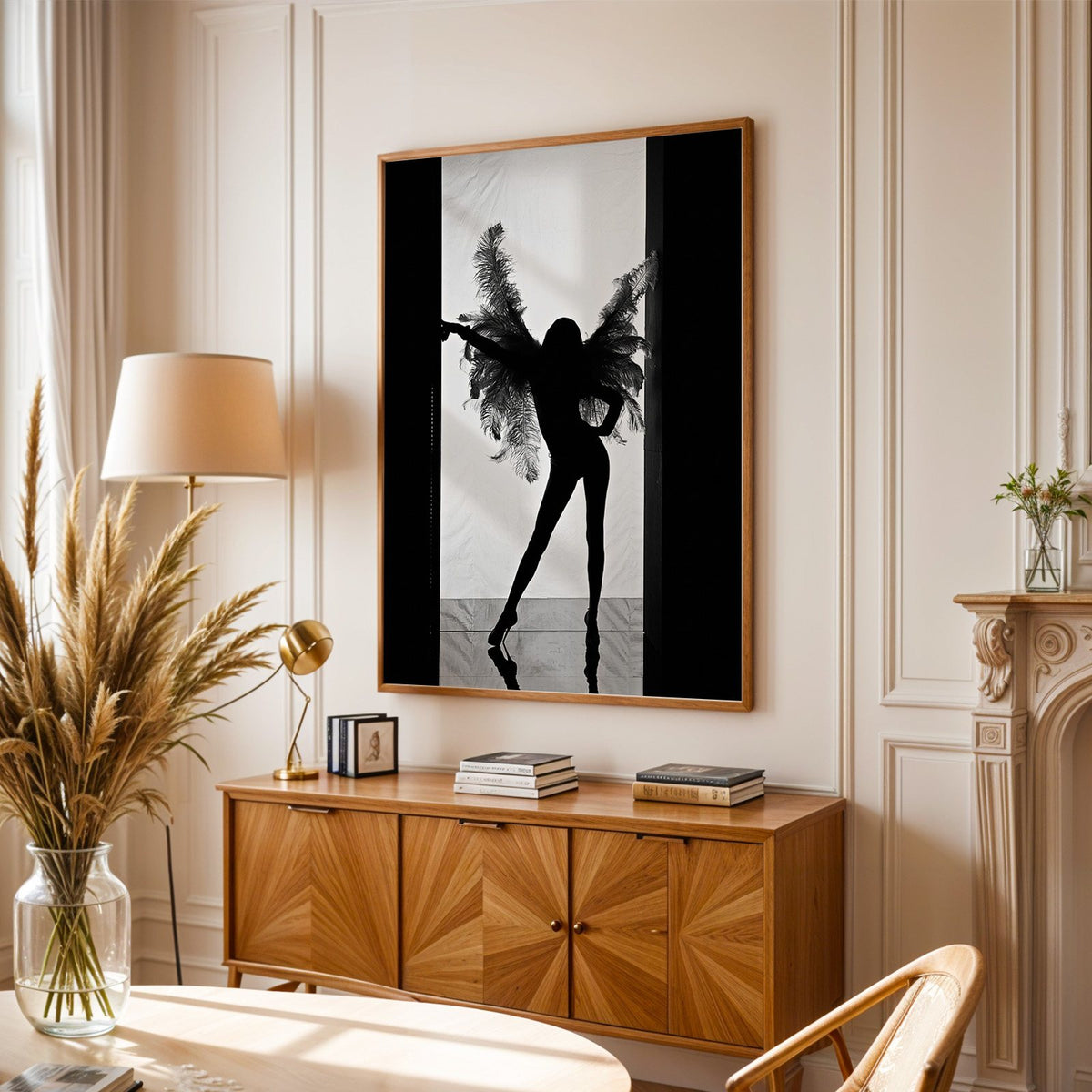 Backlit figure with feather wings in a doorway print in an oak frame above a sunburst wood sideboard with pampas grass
