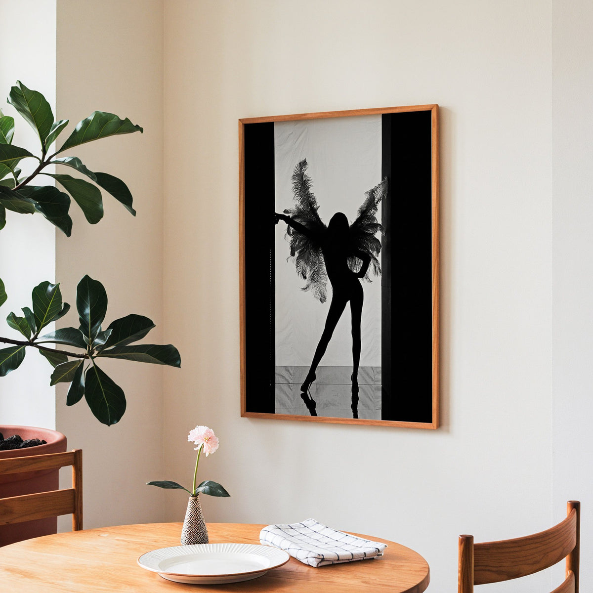 Backlit figure with feather wings in a doorway print in a teak frame above a round wooden dining table