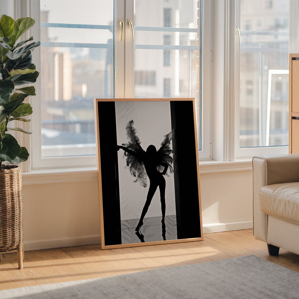 Backlit figure with feather wings in a doorway print in an oak frame leaning on the floor beside a fiddle leaf fig