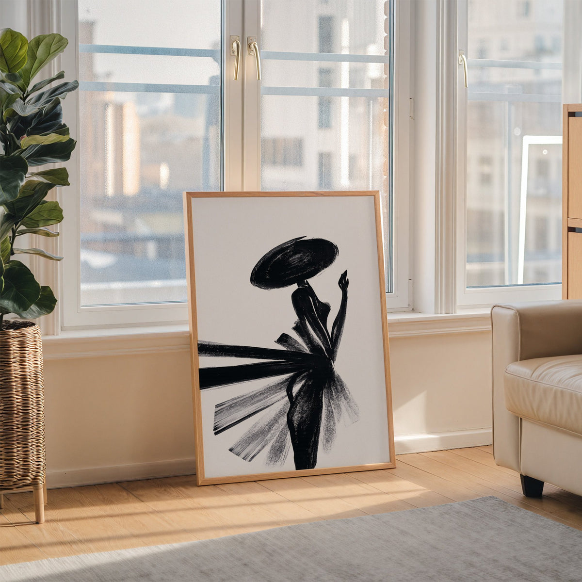 Woman in wide hat with fanned brushstroke skirt print in an oak frame leaning on the floor beside a fiddle leaf fig