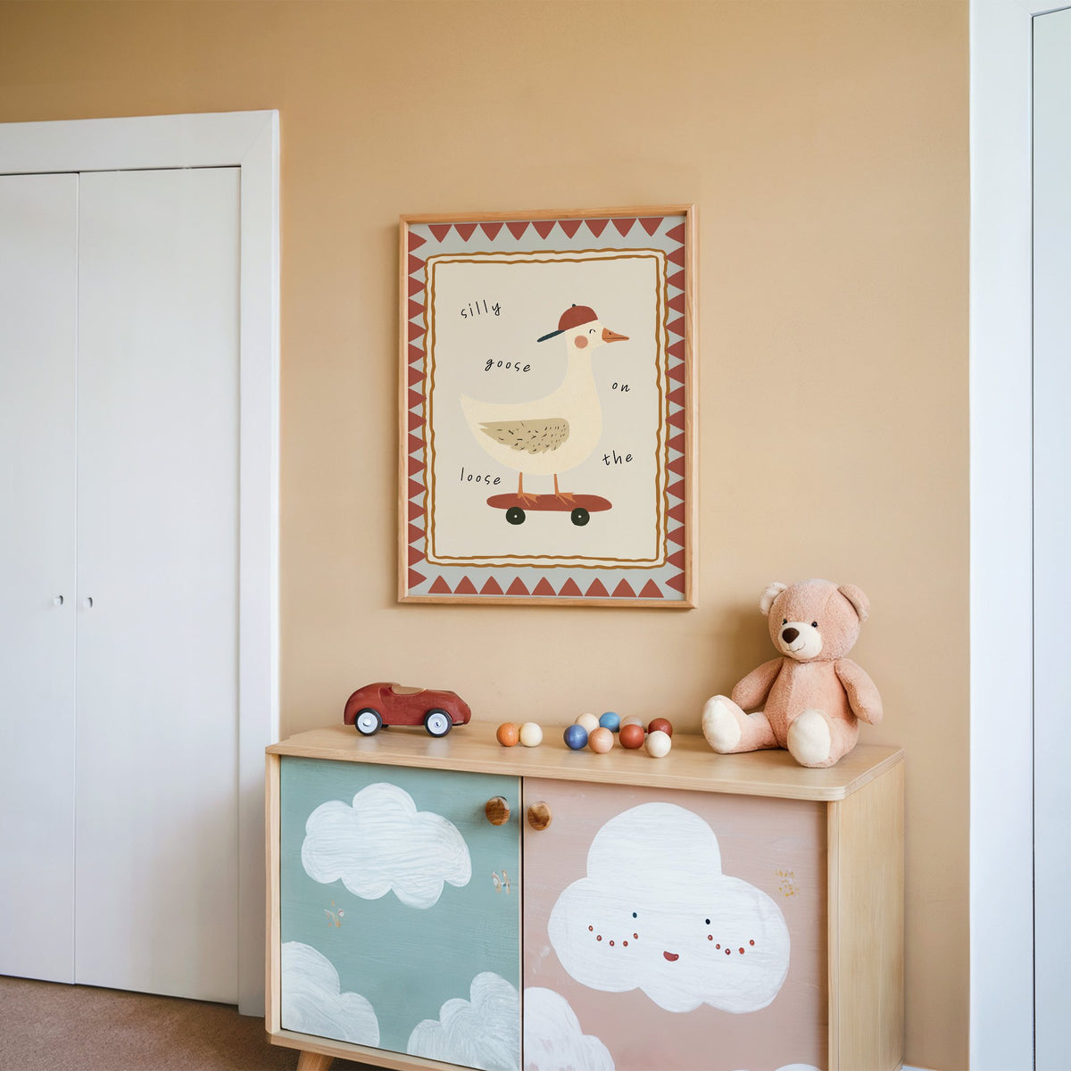 Silly goose on the loose nursery print in an oak frame on a peach wall above a cloud-painted cabinet