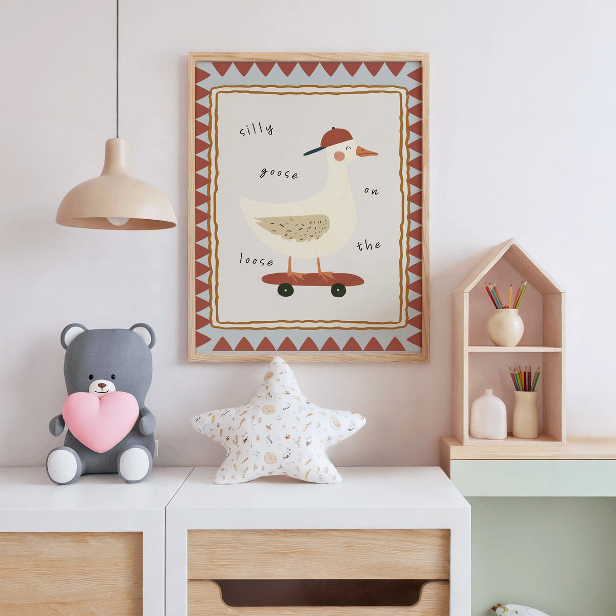 Silly goose on the loose nursery print in an oak frame above a white dresser with a star pillow and house shelf
