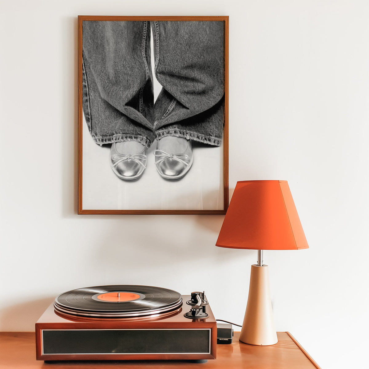 Silver ballet flats under wide-leg jeans print in a walnut frame above a record player and orange lamp