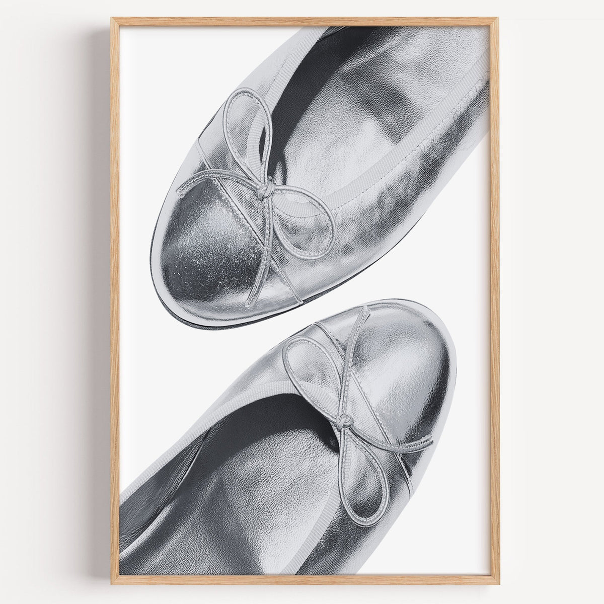 Plain toe silver ballet flats from above print in a light oak frame on a plain white wall