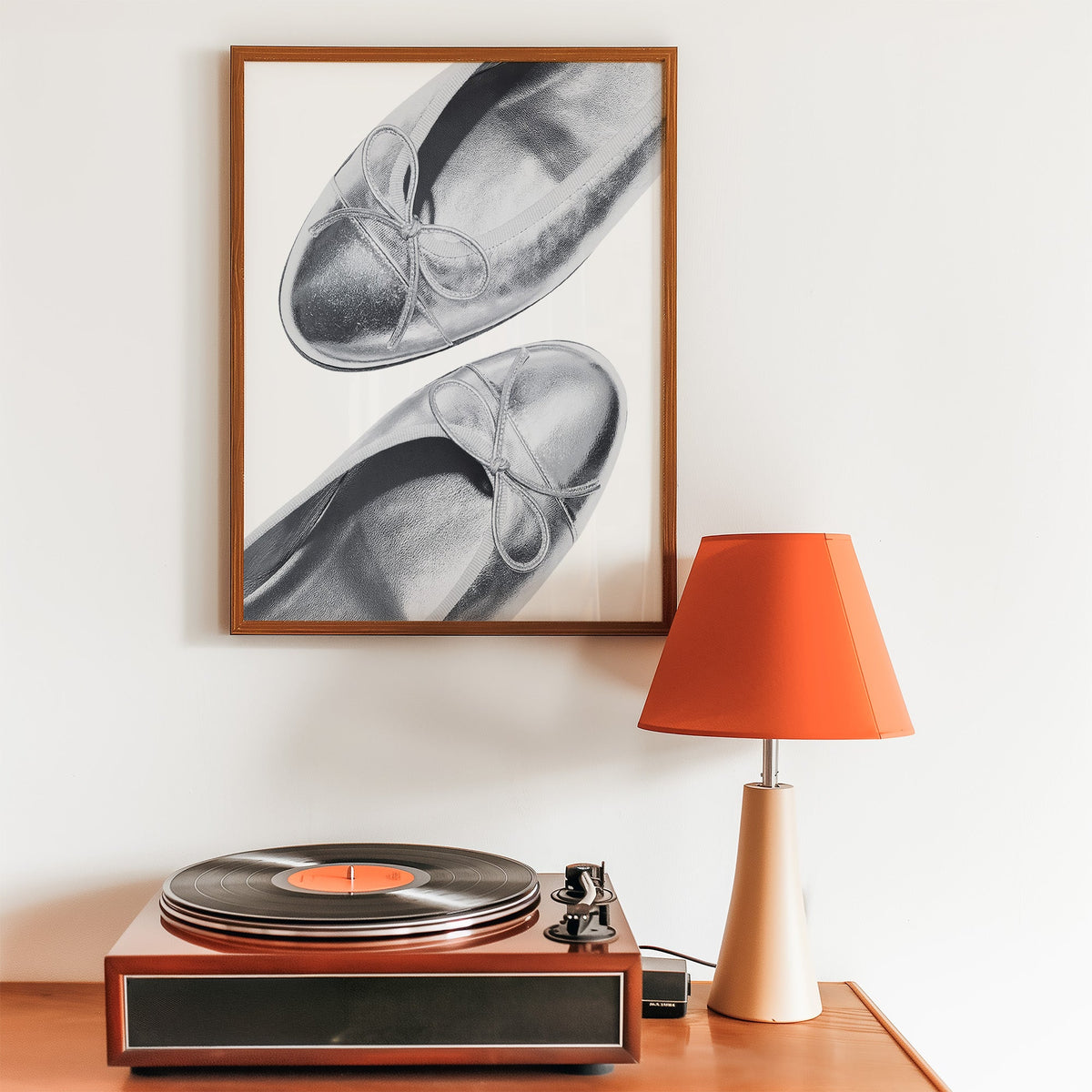 Plain toe silver ballet flats from above print in a walnut frame above a record player and orange lamp