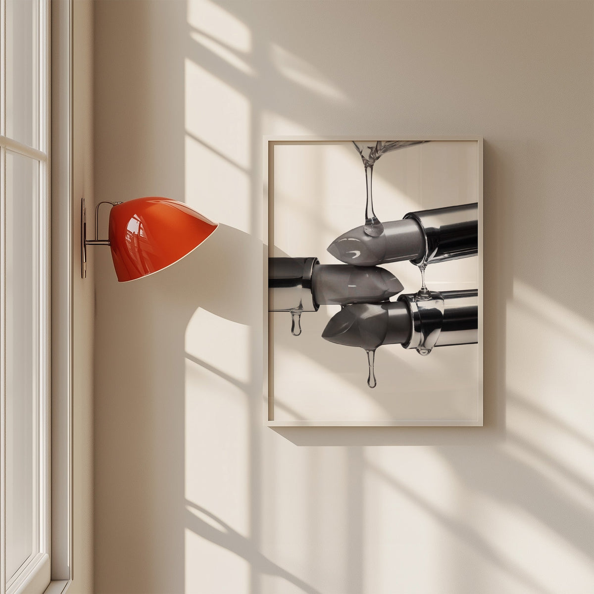 Silver lipsticks with clear gel drips print in a white frame on a sunlit wall beside a red sconce