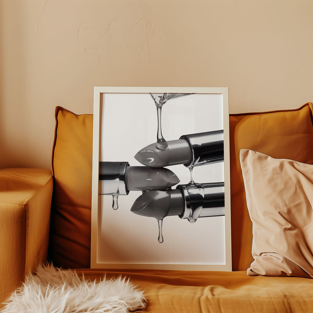 Silver lipsticks with clear gel drips print in a white frame leaning on a mustard velvet sofa