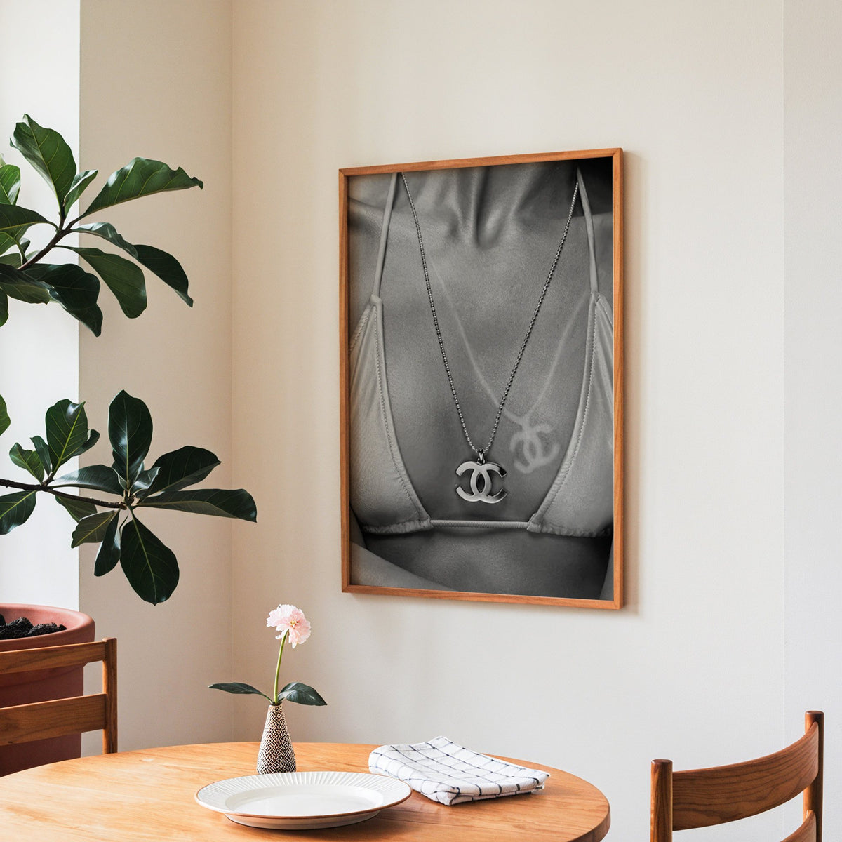 Close-up of logo pendant necklace and bikini tan line print in a teak frame above a round wooden dining table