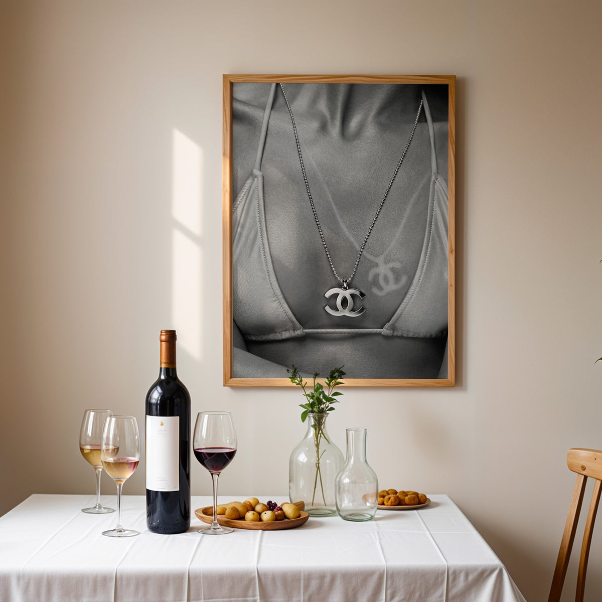 Close-up of logo pendant necklace and bikini tan line print in an oak frame above a table set with red wine and glasses