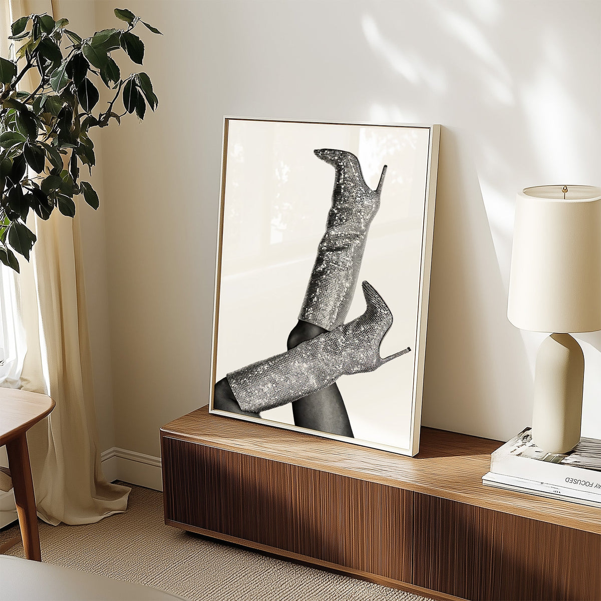Silver sequin knee-high stiletto boots print in a white frame on a walnut sideboard beside a ceramic lamp