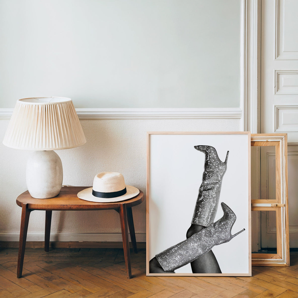 Silver sequin knee-high stiletto boots print in a pine frame on a wood floor beside a lamp and straw hat