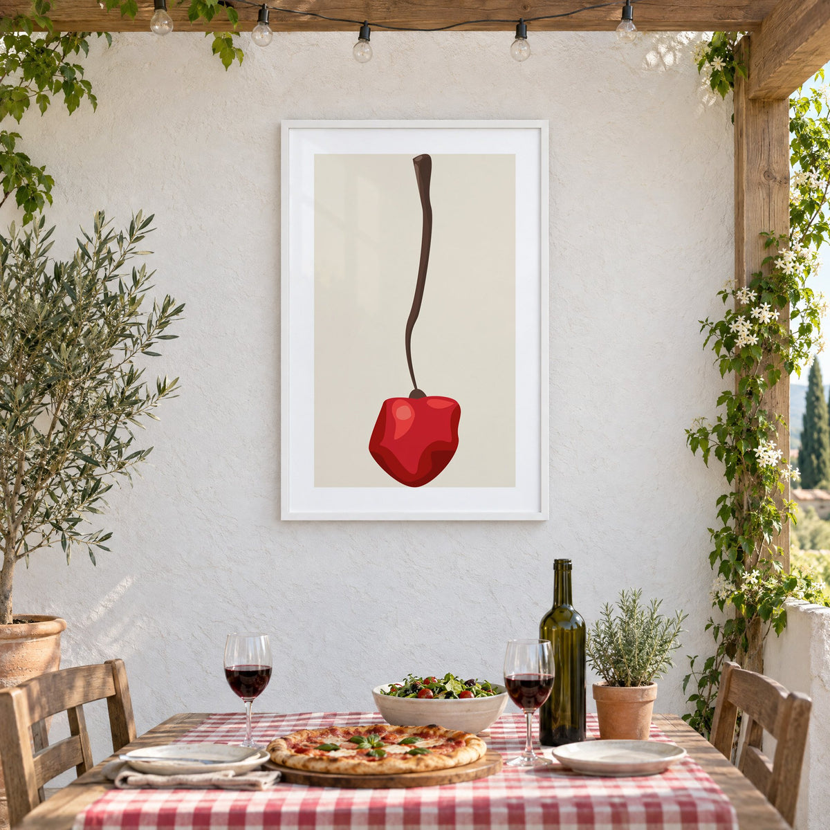 Single red cherry long stem minimalist print in a white frame on a stucco wall above a checked-cloth table with pizza and red wine