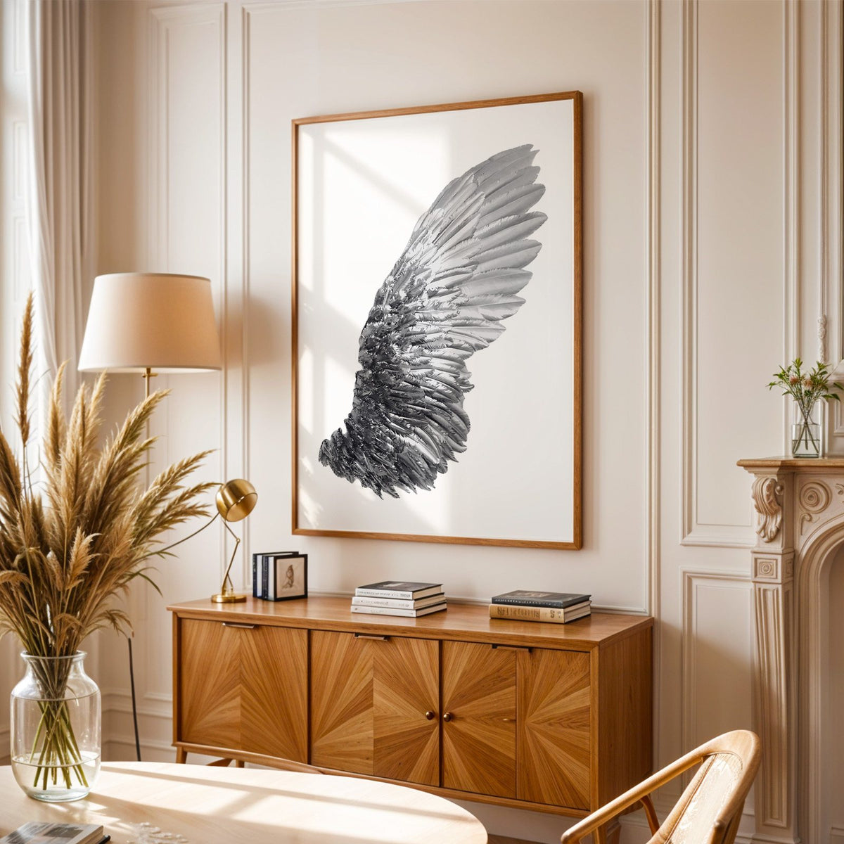 Single silver metallic wing on white print in an oak frame above a sunburst wood sideboard with pampas grass