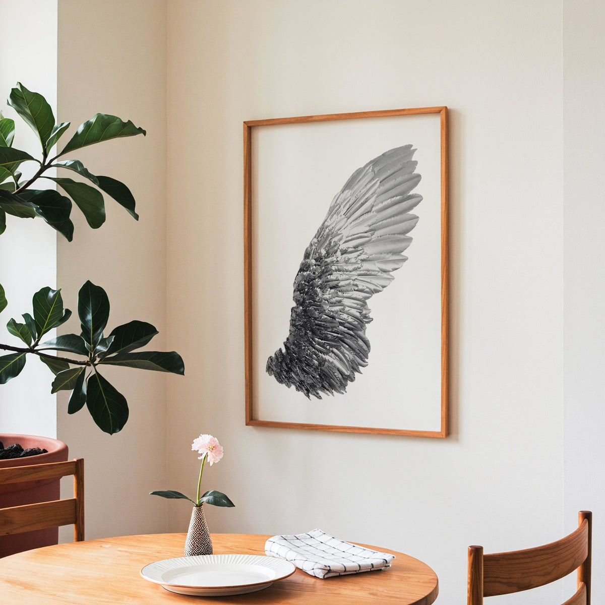 Single silver metallic wing on white print in a teak frame above a round wooden dining table