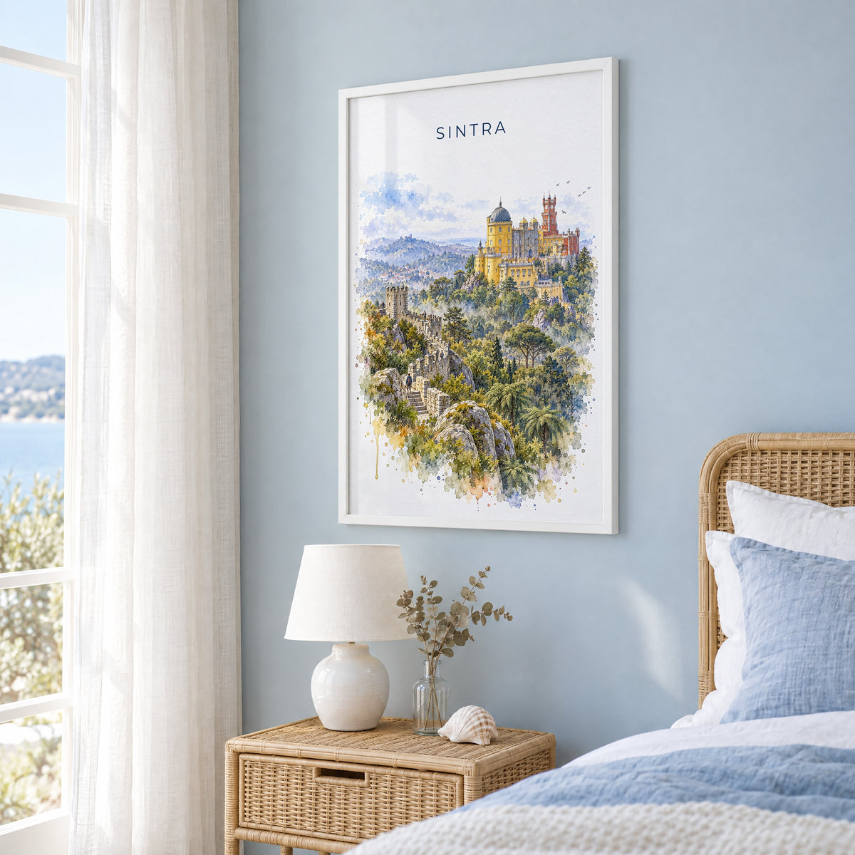 Sintra watercolor print in a white frame on a pale blue wall beside a rattan bed in a coastal bedroom