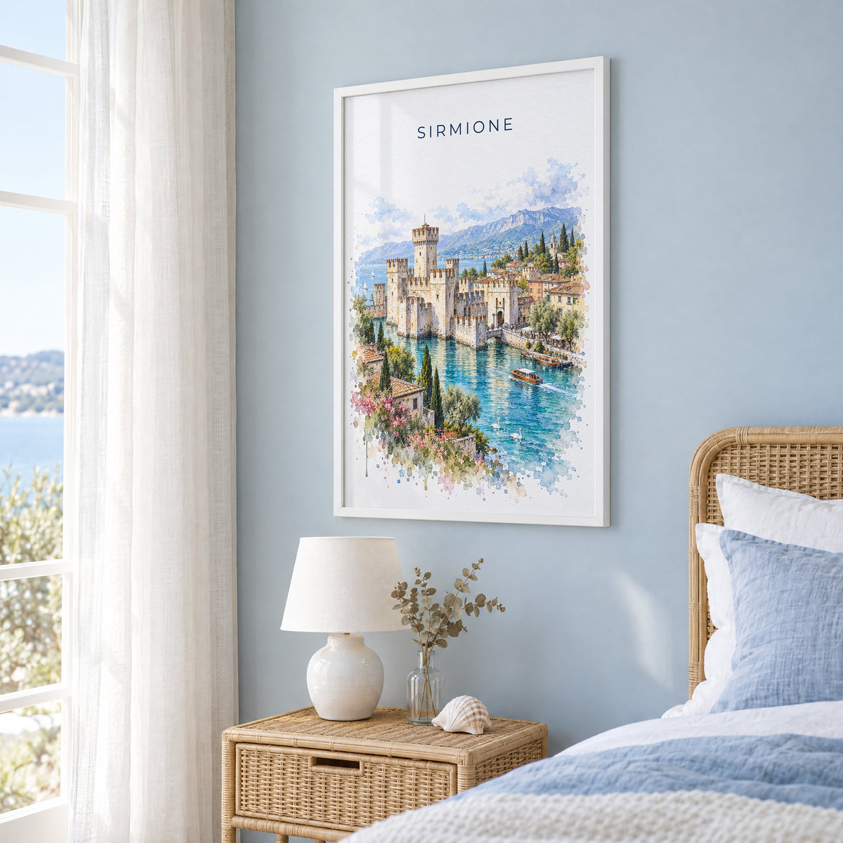 Sirmione watercolor print in a white frame on a pale blue wall beside a rattan bed in a coastal bedroom