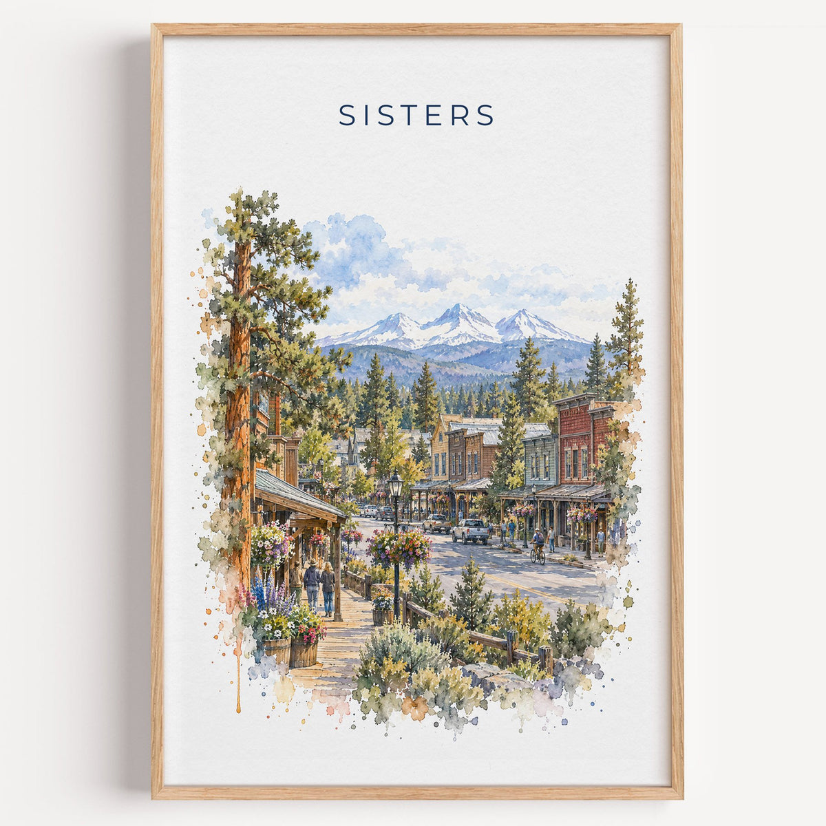 Sisters, Oregon watercolor print in a light oak frame on a plain white wall