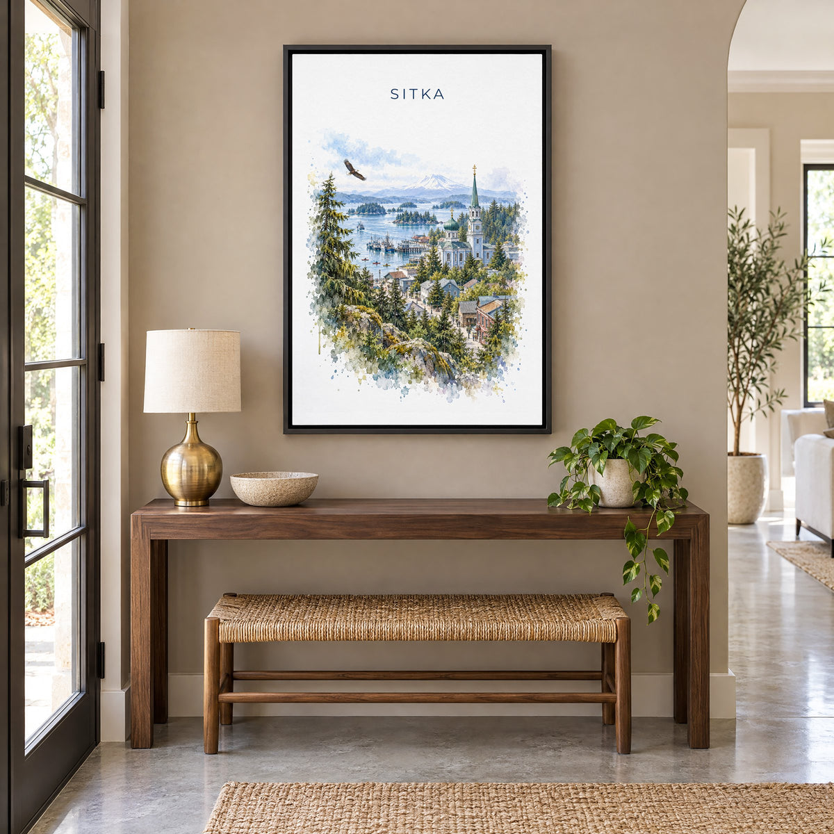Sitka, Alaska watercolor print as a black floater canvas above a walnut console and woven bench in an entryway