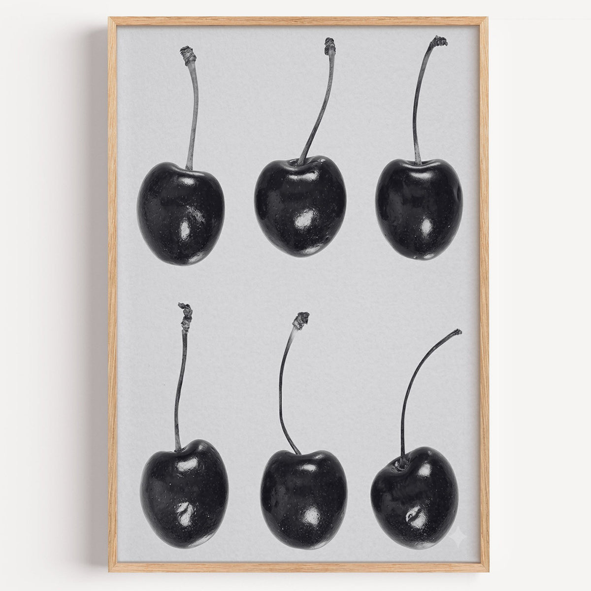Six glossy black cherries in a grid on gray print in a light oak frame on a plain white wall