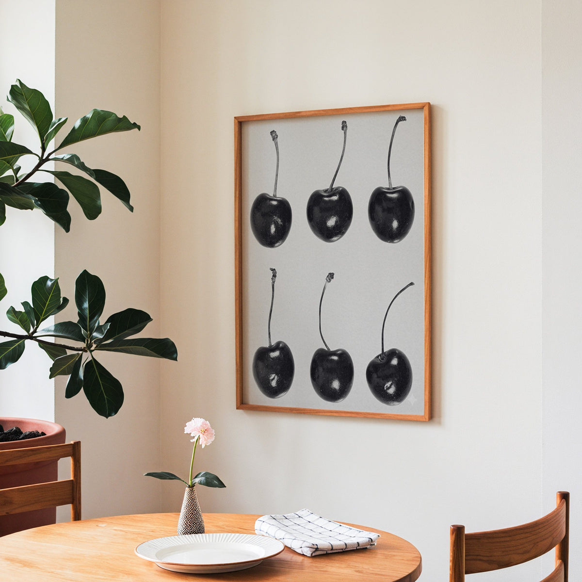 Six glossy black cherries in a grid on gray print in a teak frame above a round wooden dining table