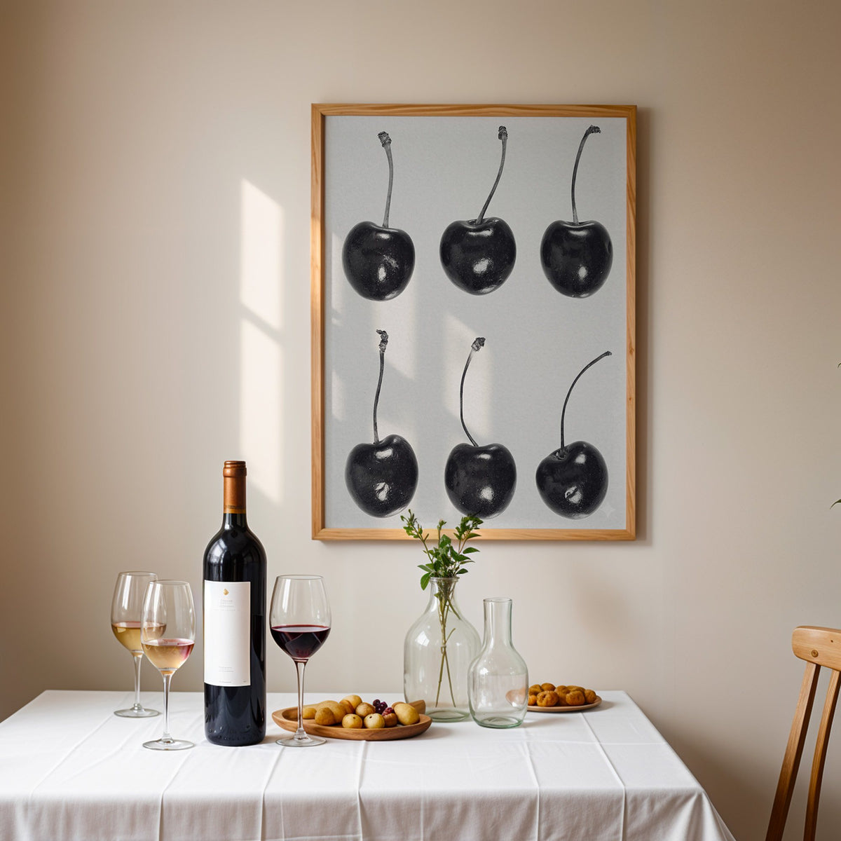 Six glossy black cherries in a grid on gray print in an oak frame above a table set with red wine and glasses