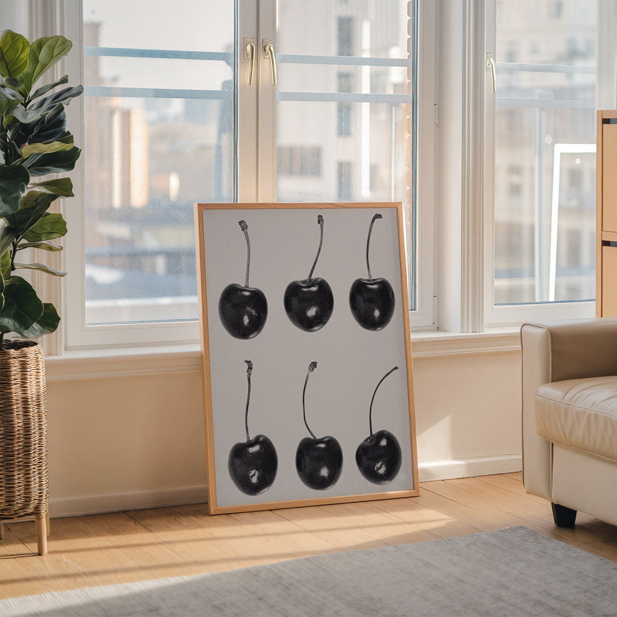 Six glossy black cherries in a grid on gray print in an oak frame leaning on the floor beside a fiddle leaf fig