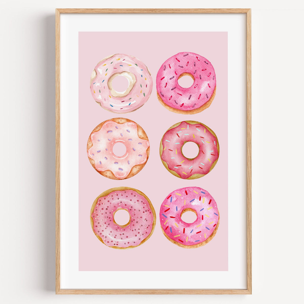 Six pink watercolor donuts print in a light oak frame on a plain white wall