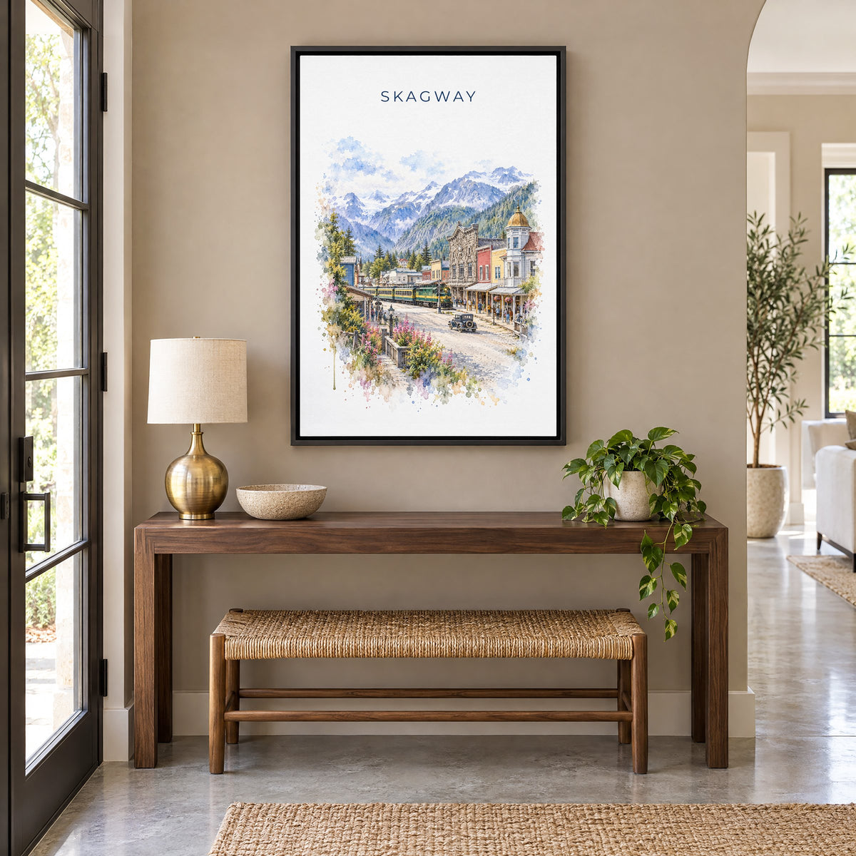 Skagway, Alaska watercolor print as a black floater canvas above a walnut console and woven bench in an entryway