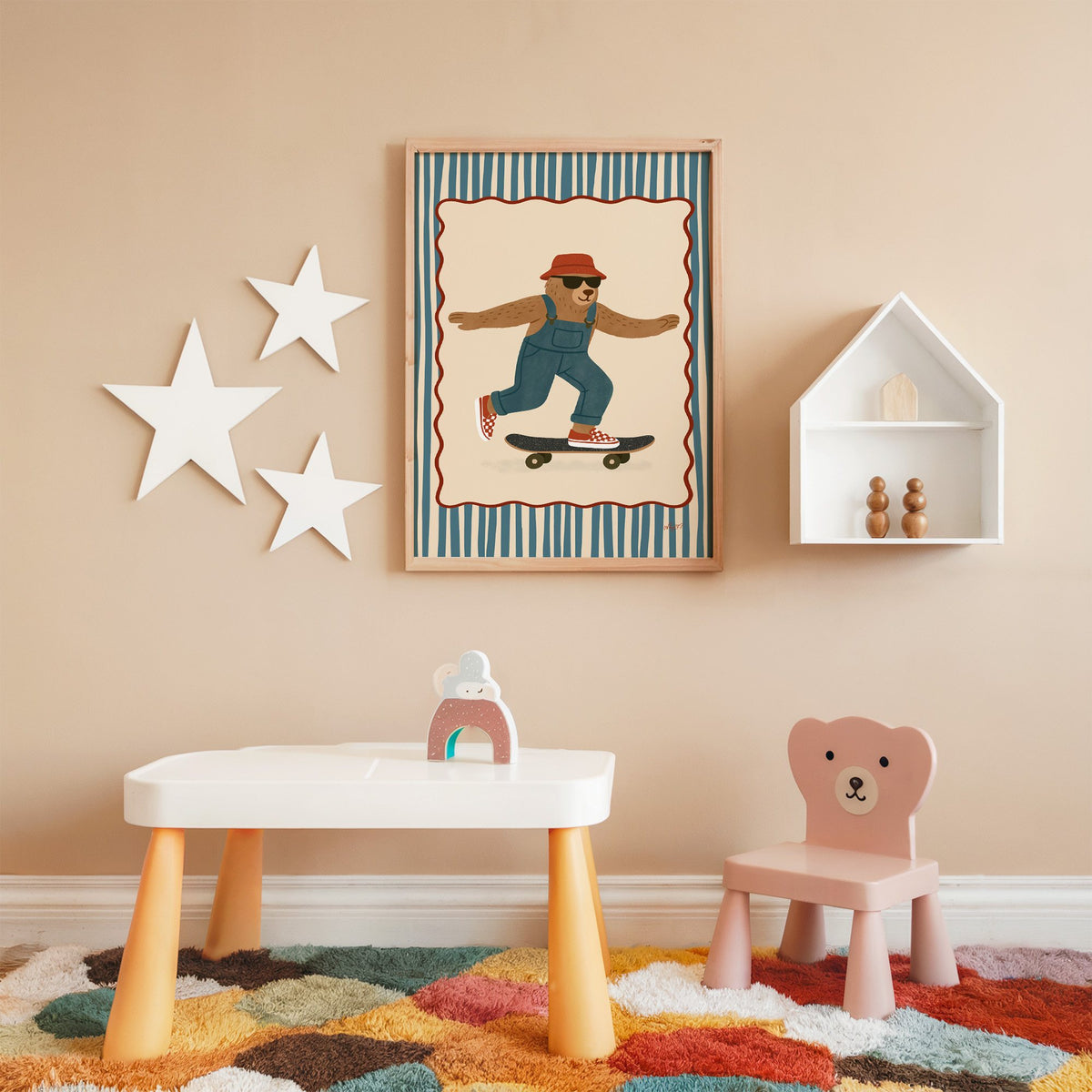 Bear in overalls on a skateboard nursery print in an oak frame on a peach wall above a kids table with wall stars