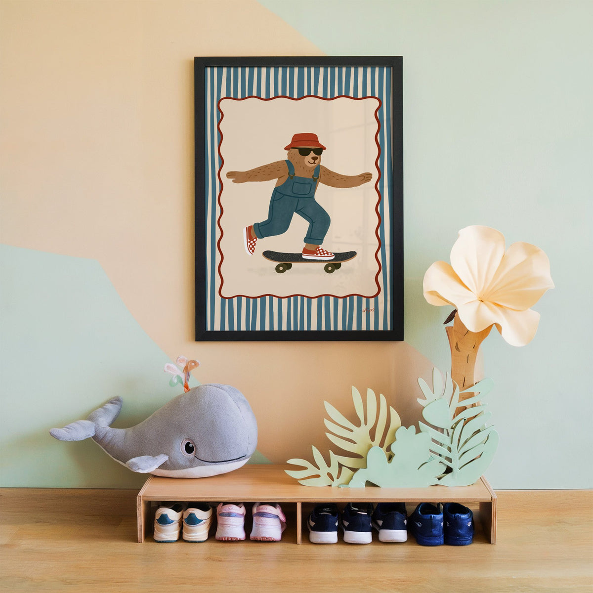 Bear in overalls on a skateboard nursery print in a black frame on a mint and peach wall above a whale plush