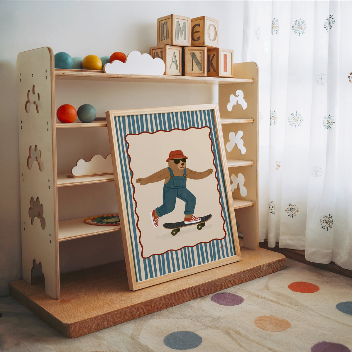 Bear in overalls on a skateboard nursery print in an oak frame leaning on a toy shelf with wooden letter blocks