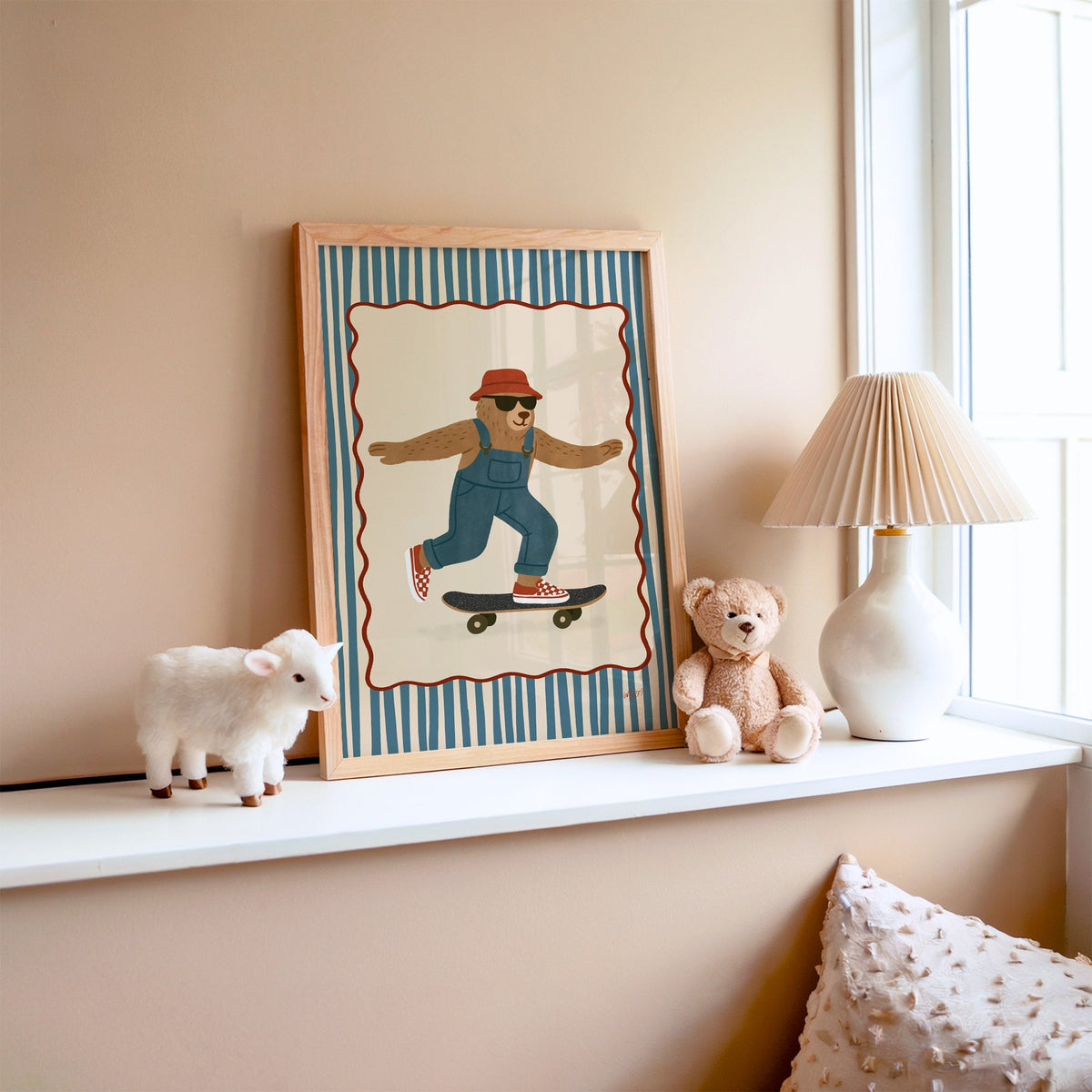 Bear in overalls on a skateboard nursery print in an oak frame on a window ledge with a toy lamb and teddy