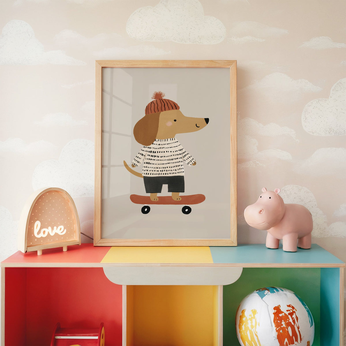 Skateboard dog pompom beanie nursery print in an oak frame on a rainbow toy shelf against cloud wallpaper