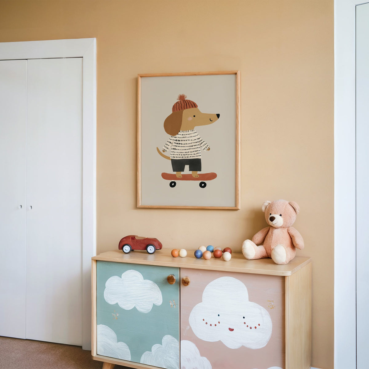 Skateboard dog pompom beanie nursery print in an oak frame on a peach wall above a cloud-painted cabinet