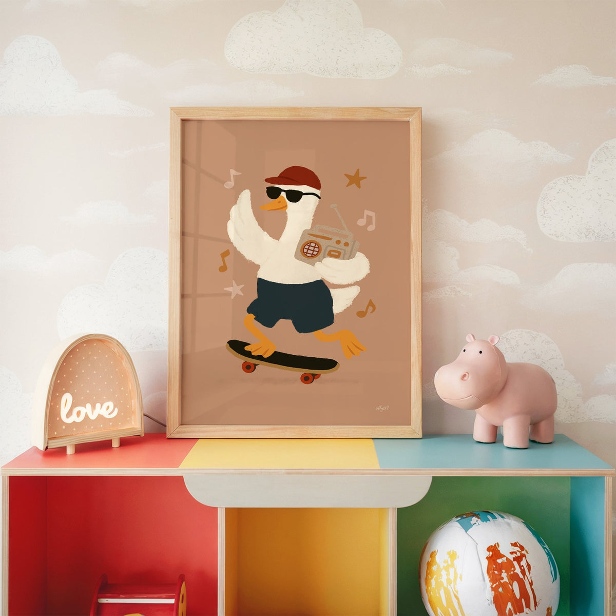 Goose on skateboard with boombox nursery print in an oak frame on a rainbow toy shelf against cloud wallpaper