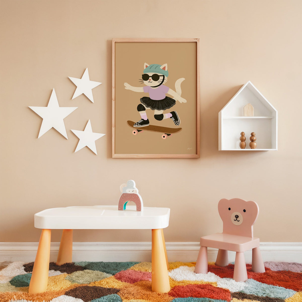 Skater cat in black tutu nursery print in an oak frame on a peach wall above a kids table with wall stars