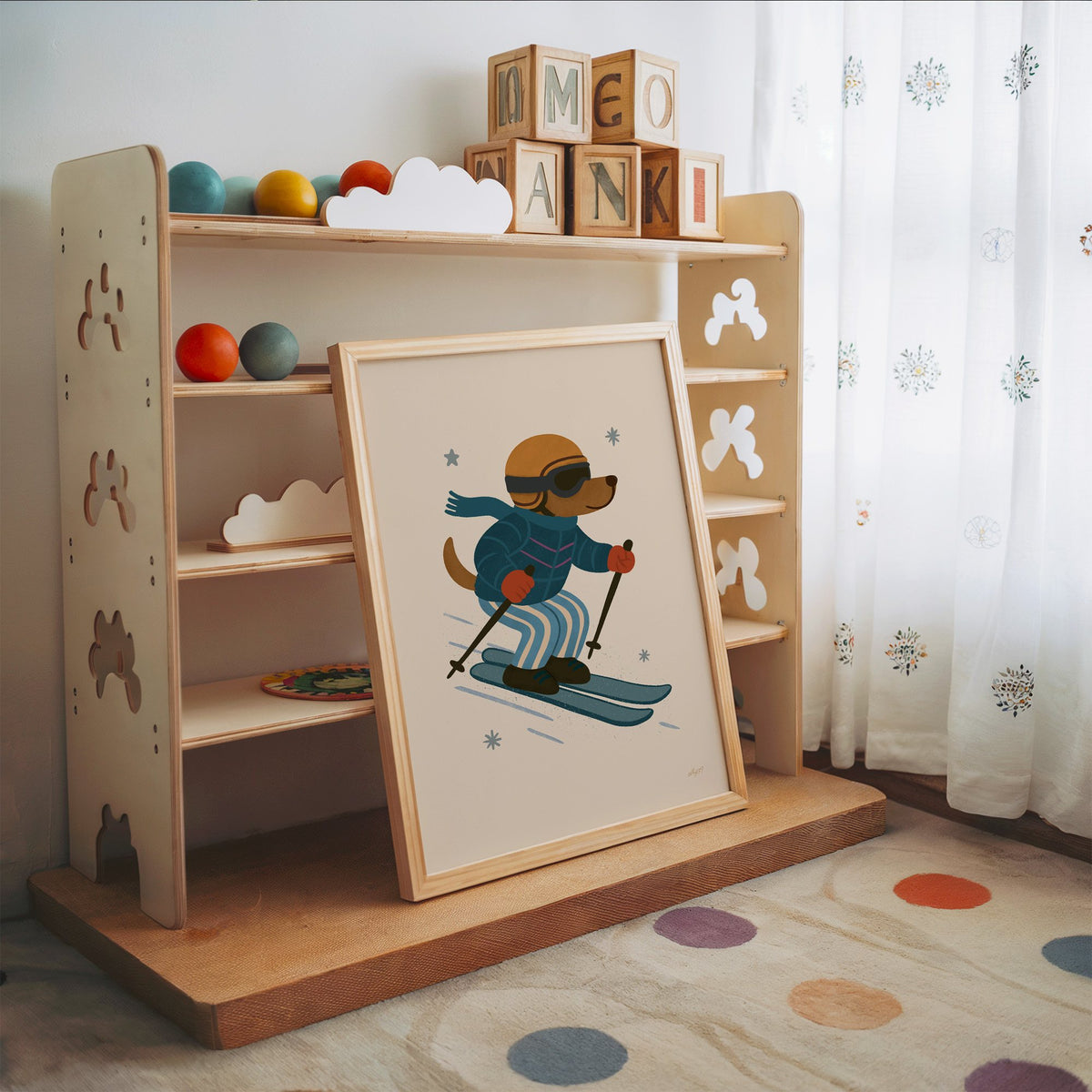 Skiing dog in puffer jacket nursery print in an oak frame leaning on a toy shelf with wooden letter blocks