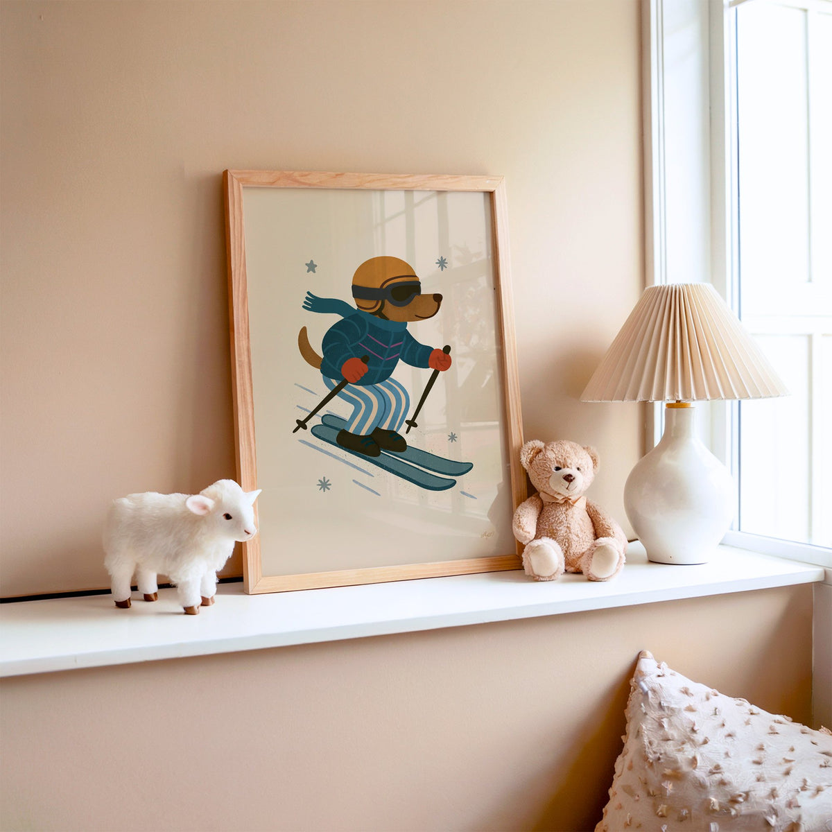 Skiing dog in puffer jacket nursery print in an oak frame on a window ledge with a toy lamb and teddy