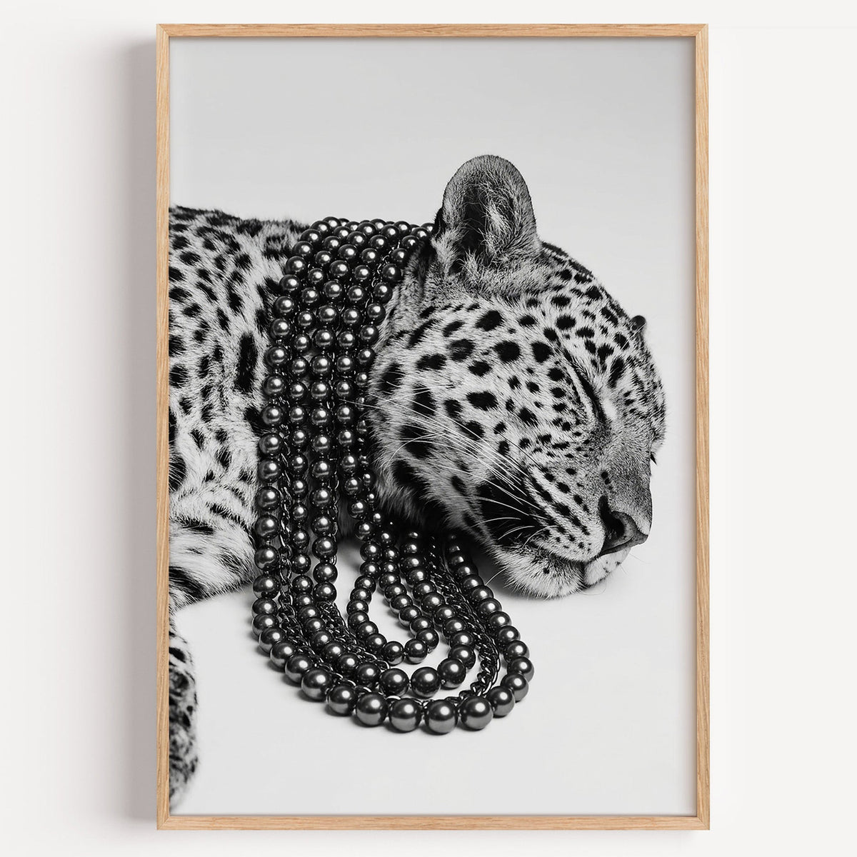 Sleeping leopard wearing black pearl strands print in a light oak frame on a plain white wall