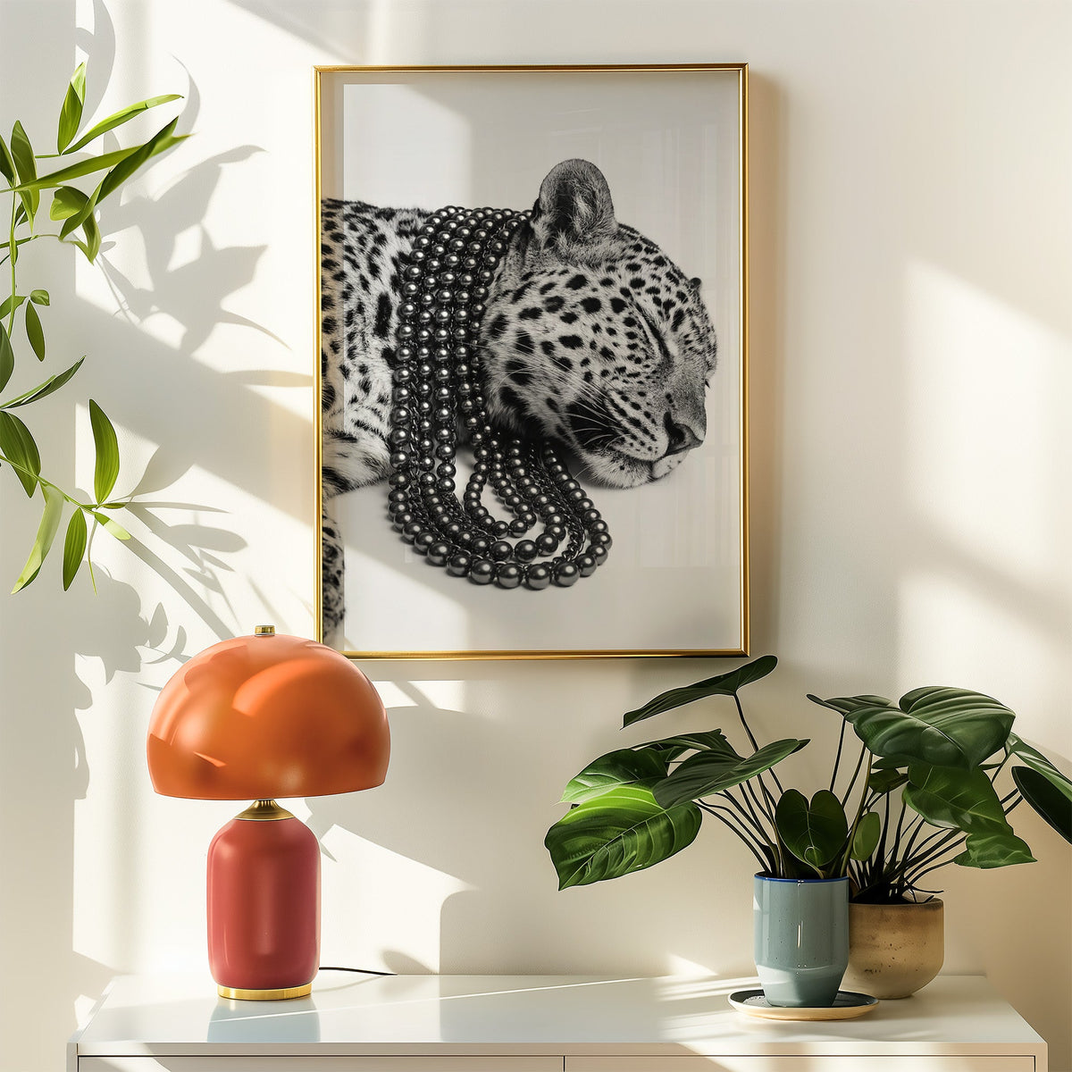 Sleeping leopard wearing black pearl strands print shown in a gold frame above a white sideboard with an orange lamp