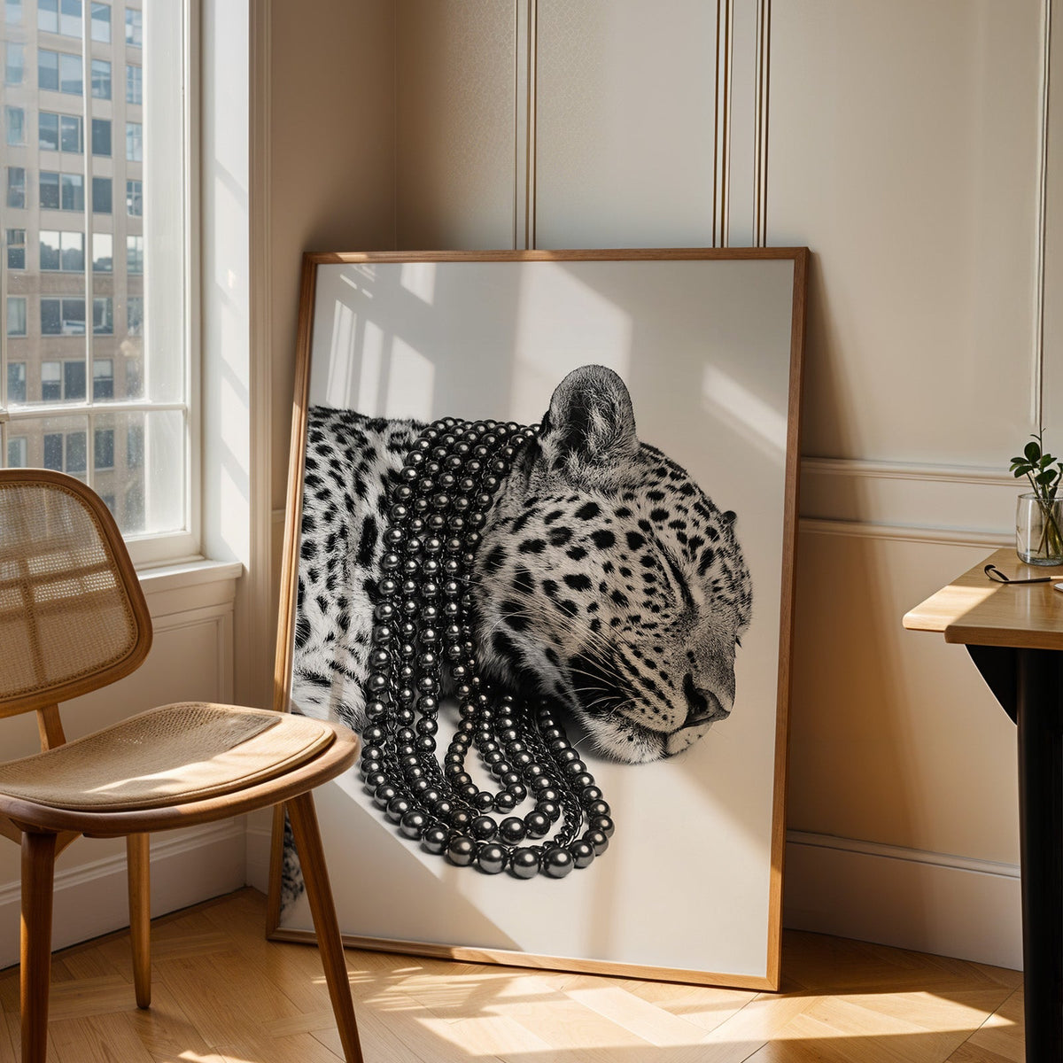 Sleeping leopard wearing black pearl strands print in an oak frame leaning in a sunlit corner beside a cane chair
