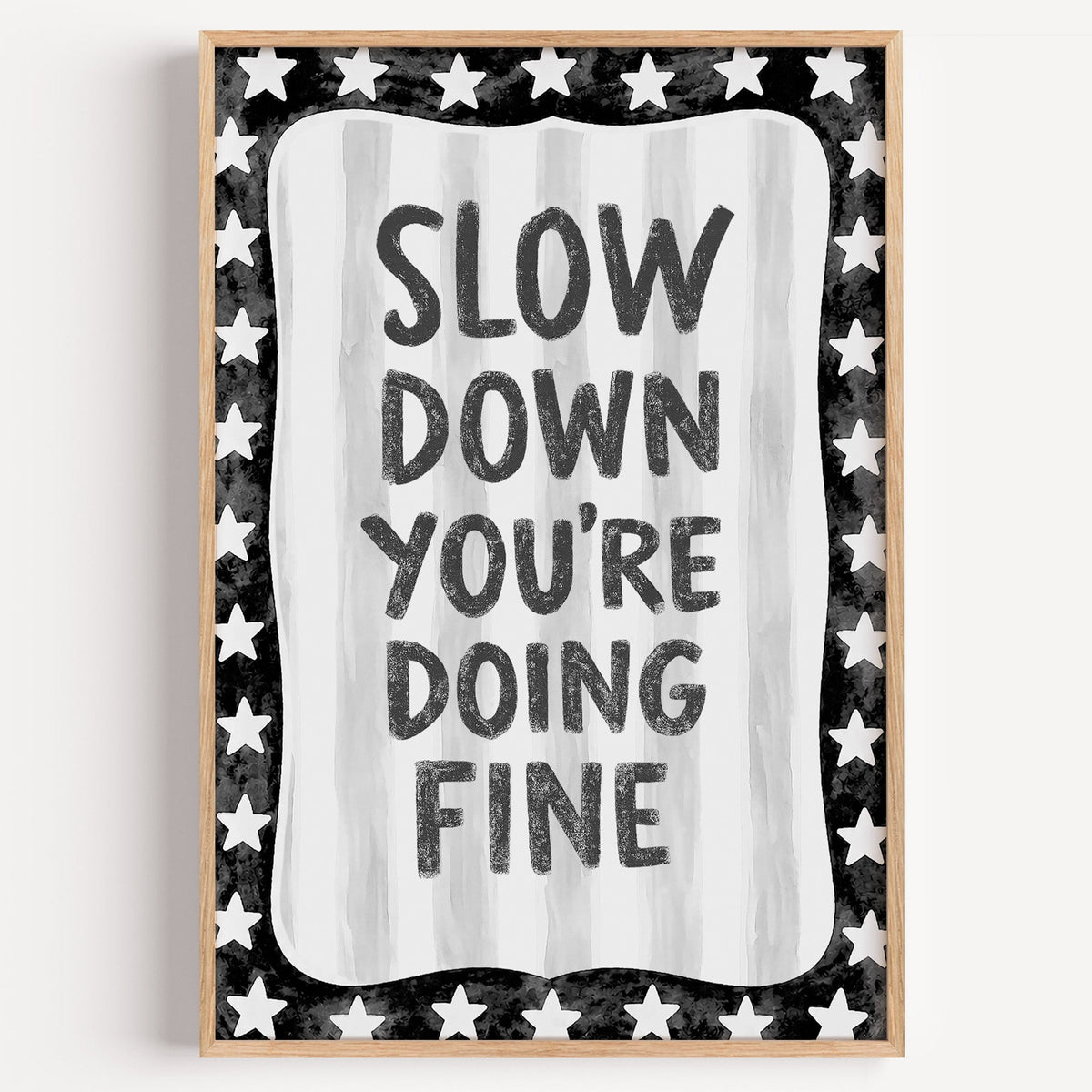 Slow down you're doing fine quote with star border print in a light oak frame on a plain white wall