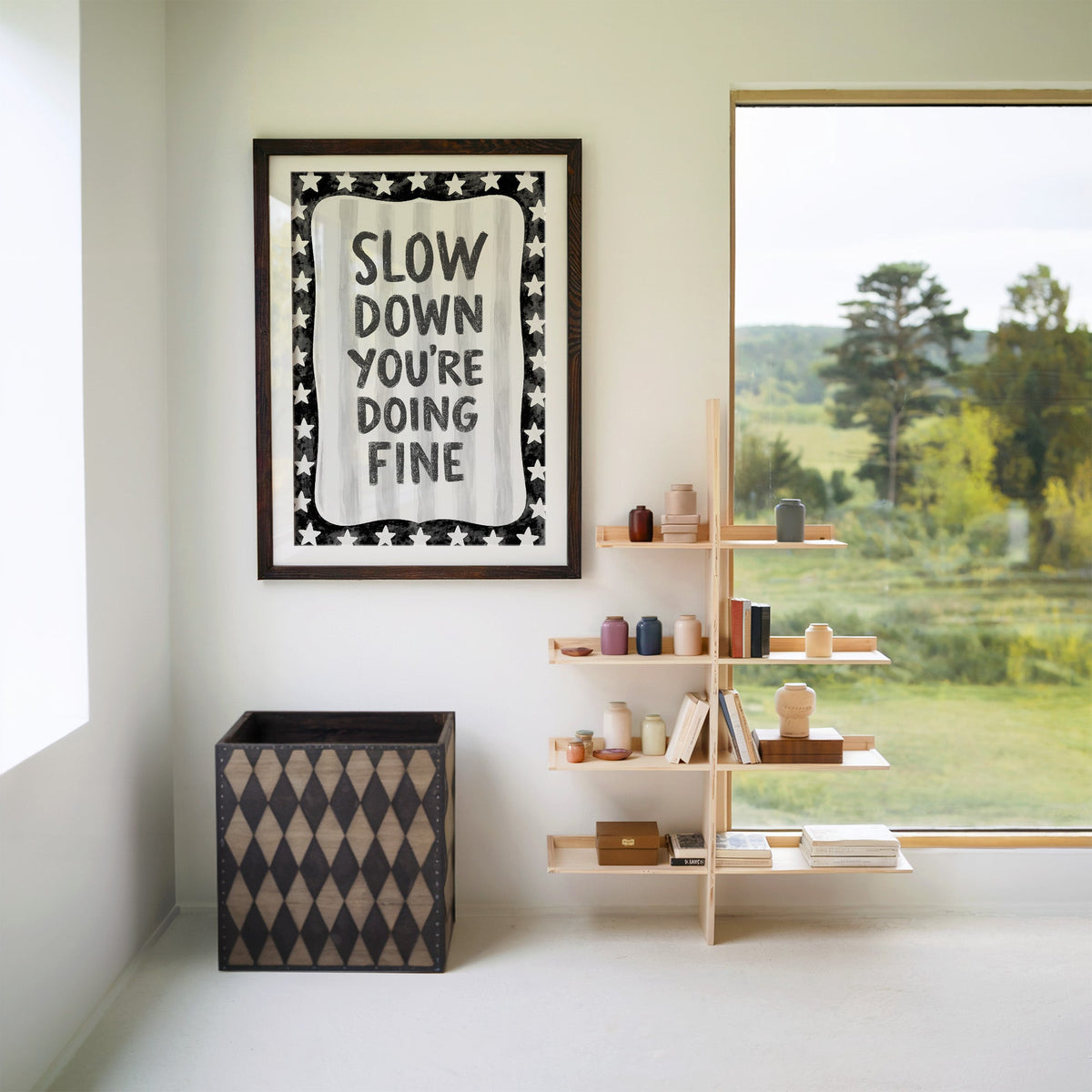 Slow down you're doing fine quote with star border print in a walnut frame with a white mat beside wooden shelves and a garden window