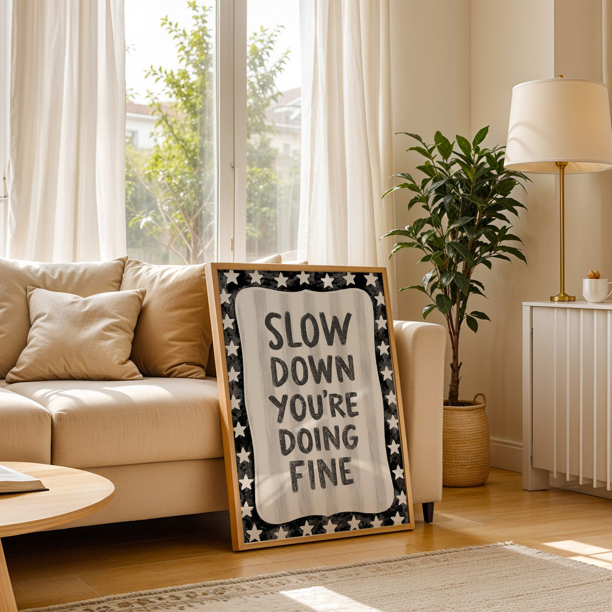Slow down you're doing fine quote with star border print in a light oak frame leaning on a cream sofa beside a floor lamp